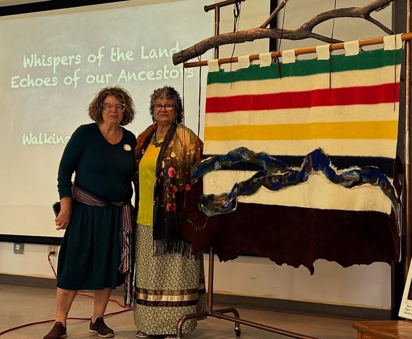 Two people standing next to art display of Hudson Bay blanket.