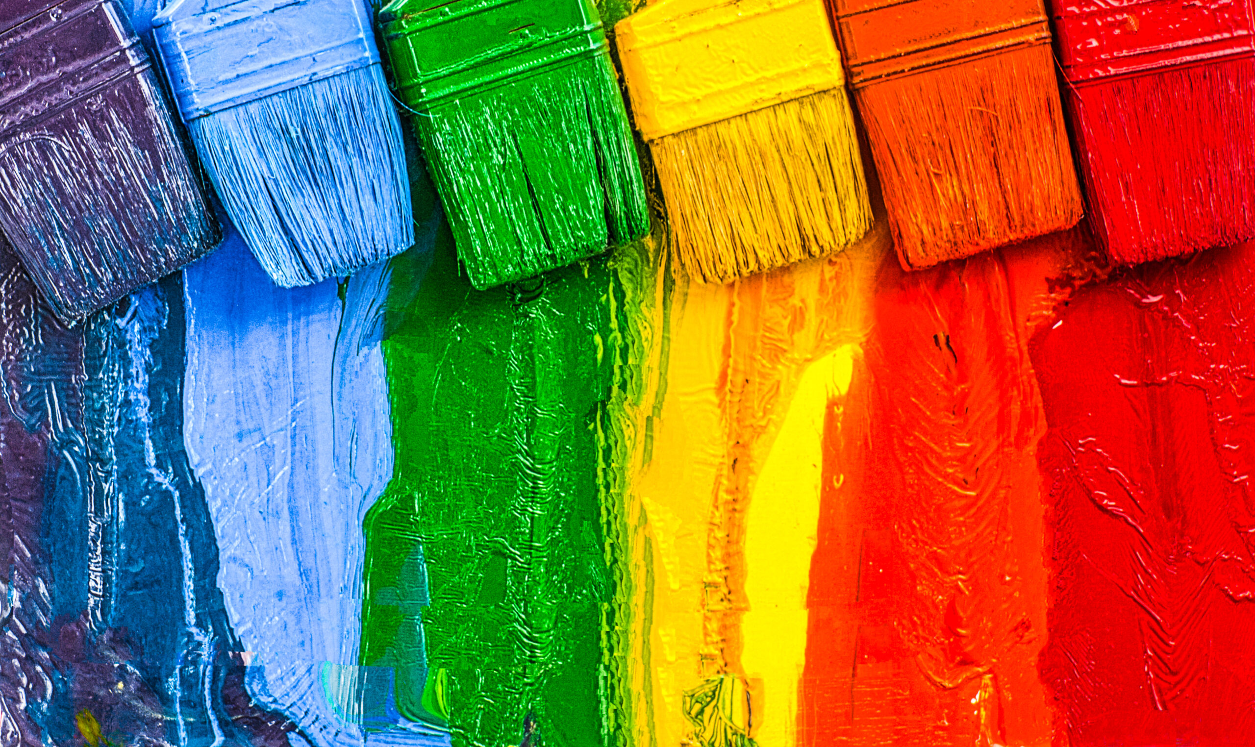 Six paint brushes and paint covered in the colours of a rainbow.