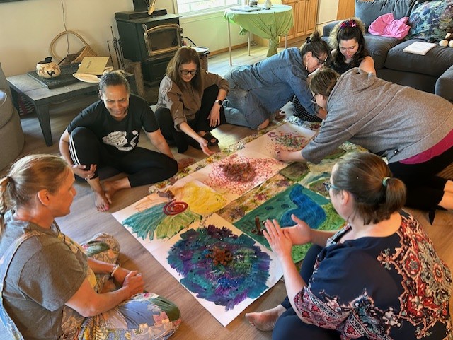Group of people sitting on the floor painting on pieces of paper.