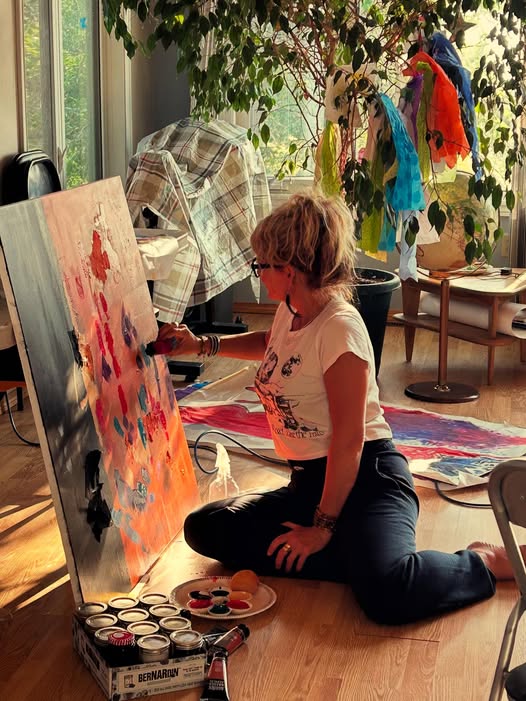 Person sitting on floor painting on a canvas.