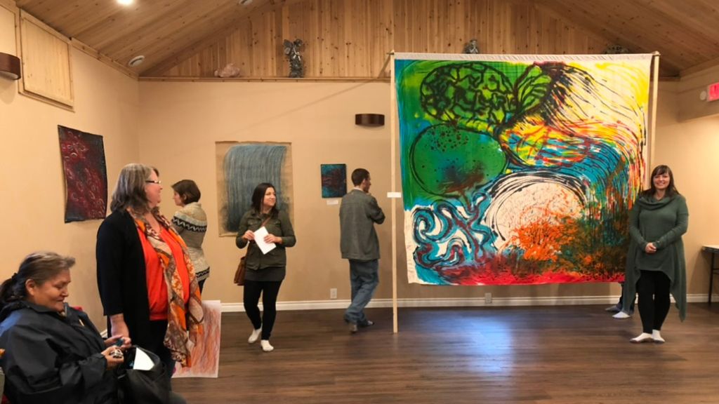 Group of people in a room with art pieces on the walls and one large art piece displayed on floor.