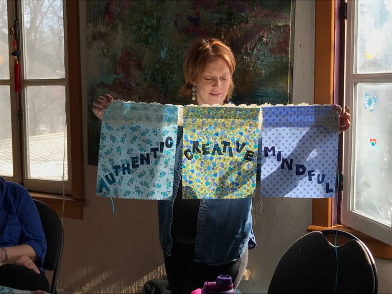 Person holding up three pieces of fabric. Text on fabric says "Authentic, Creative, Mindful"