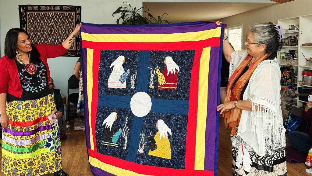 Two people holding up handmade blanket.