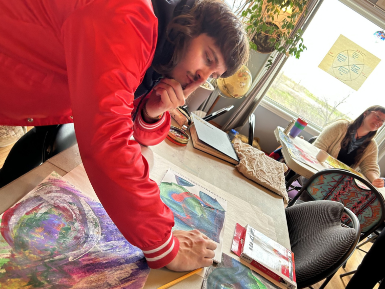 Person leaning over a table working on a painting.