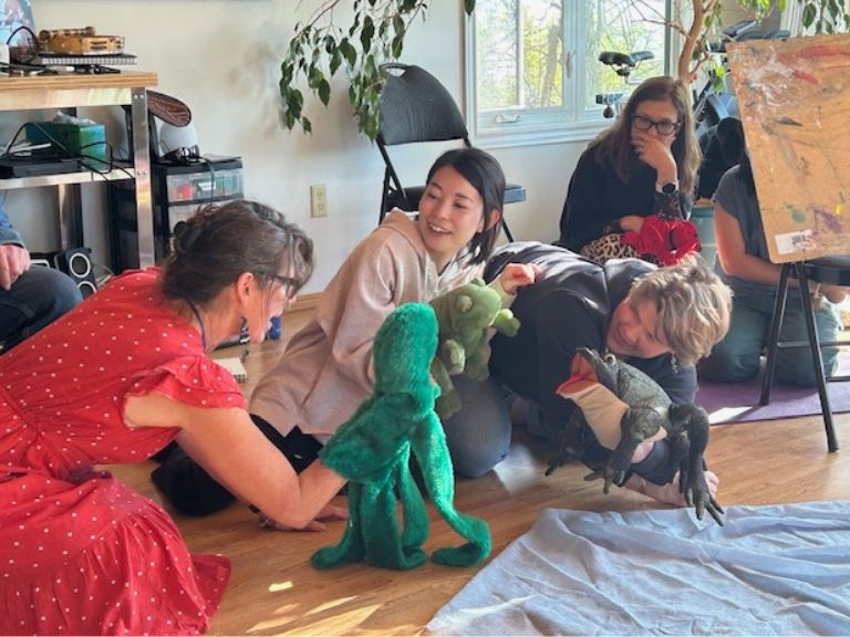 Two people sitting on floor using puppets.