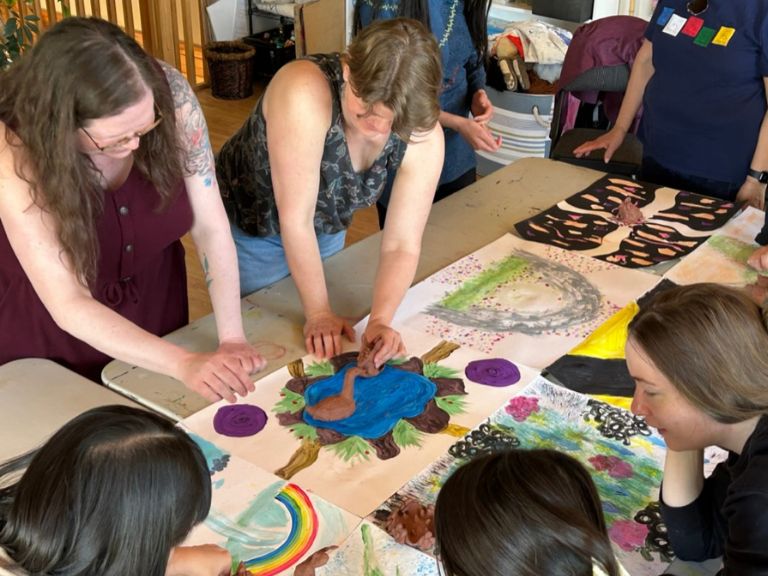 Group of people standing over table working on art project.