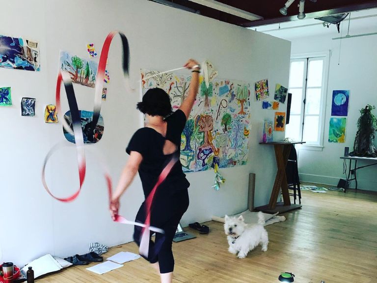 Person holding streamers dancing around room with art on the walls.