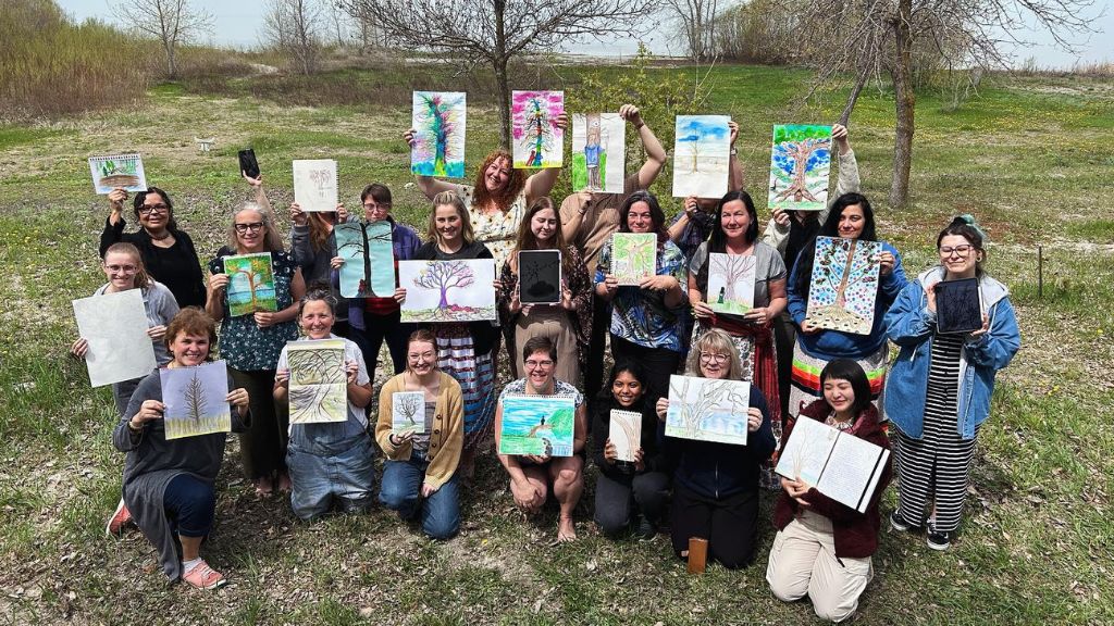Group of people outside holding up paintings of trees.