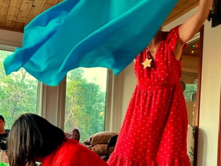 Person wearing a red dress standing and holding a blue piece of fabric.