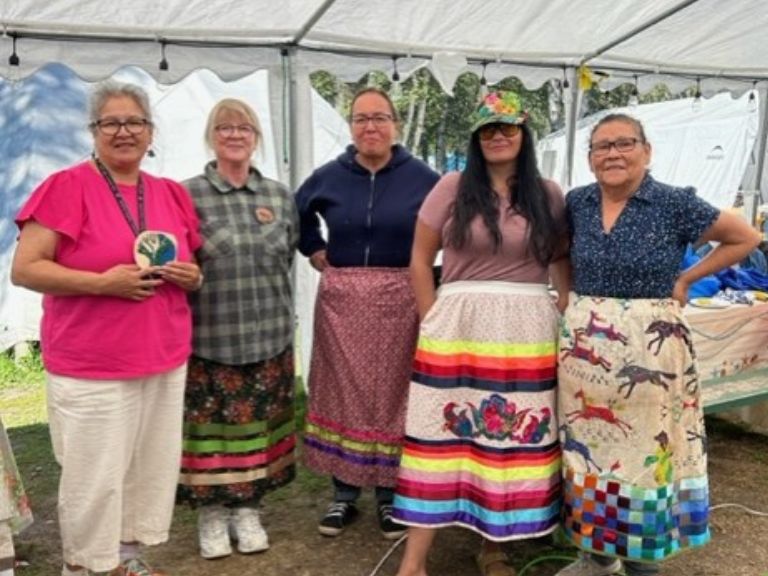 Group of people standing and wearing ribbon skirts.