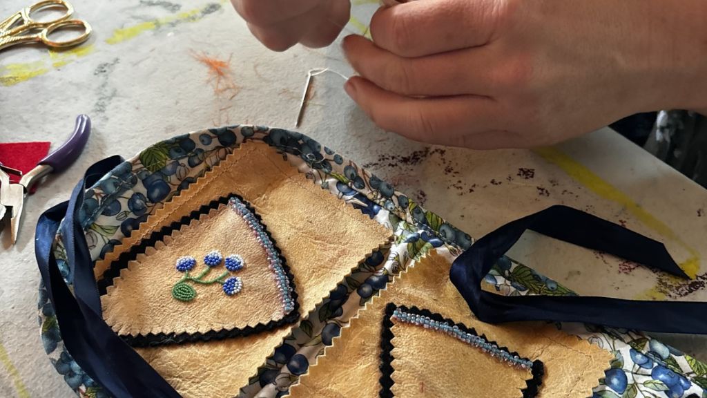 Person beading Indigenous floral pattern on material.