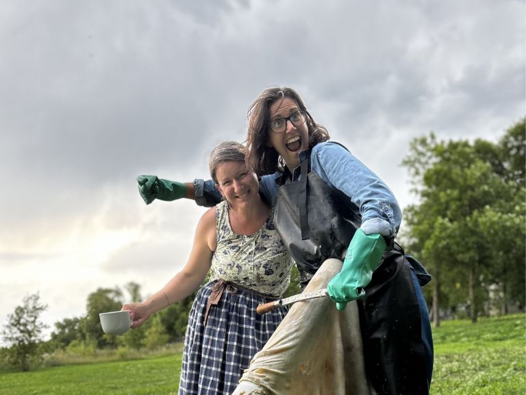 Two people standing outside together, one holding a mug and one holding a paint brush.