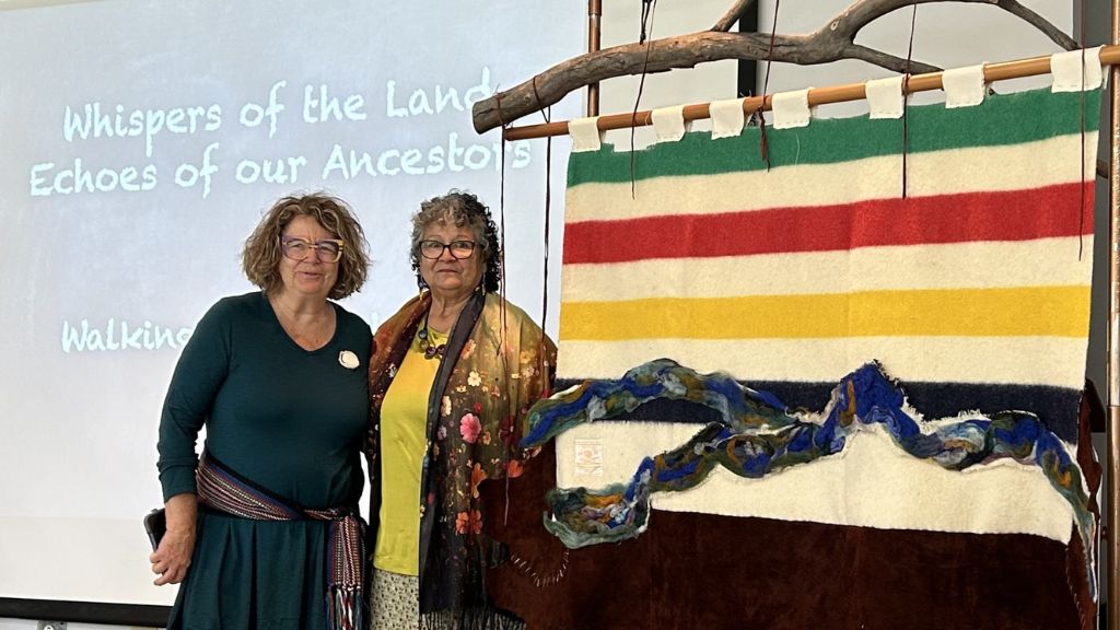 Two people standing by Hudson bay blanket art piece on display.
