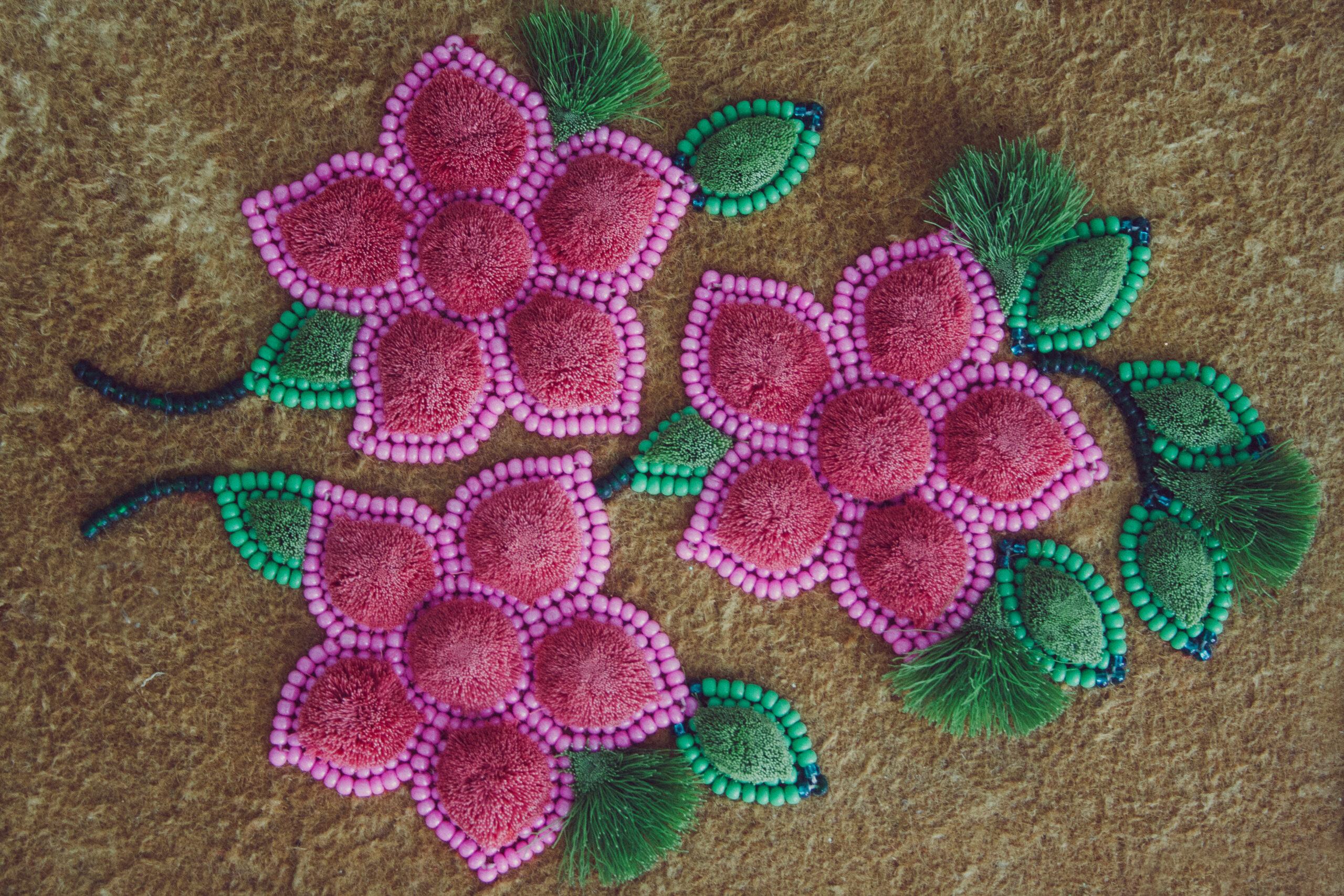 Pink beaded flowers and moose hair tufting on leather with green leaves.
