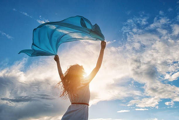 A woman on sunset background with blue scarf held to sky